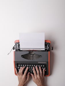 From above crop person using vintage black and red typewriter with white blank sheet of paper against white background